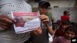 Palestinians hold leaflets dropped by Israeli planes calling on them to evacuate ahead of an Israeli military operation in Rafah, southern Gaza Strip, May 6, 2024.