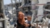 Seorang perempuan Palestina menggendong putrinya saat berjalan melewati puing-puing rumah yang hancur akibat serangan militer Israel, di Khan Younis di selatan Jalur Gaza, 10 Juli 2024. (REUTERS/Hatem Khaled)