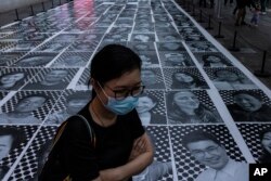 FILE - A pedestrian passes smiling portraits on display as part of the installation titled "Inside Out: Harbour and the City" created by French artist JR in Hong Kong, April 26, 2023.