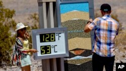 Tourists take photographs with the thermometer at the Furnace Creek Visitor Center during a dangerous heat wave, July 9, 2024, in Death Valley, Calif.