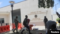FILE - A man carries his belongings after officers of the Haitian National Police fired tear gas to clear a camp of people escaping the threat of armed gangs, in front of the U.S. Embassy, in Port-au-Prince, Haiti, July 25, 2023. 