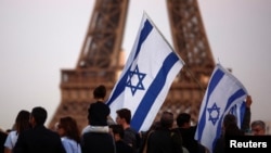 Supporters of Israel hold flags as they protest following Hamas' biggest attack on Israel in years, in Paris, France, Oct. 9, 2023, with the Eiffel Tower in the background.