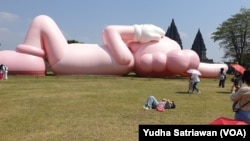 Para pengunjung sedang memperhatikan boneka balon raksasa berbentuk kelinci berwarna merah muda karya pekerja seni asal AS, KAWS, di Candi Prambanan, Sleman, Yogyakarta, Kamis, 24 Agustus 2023. (Foto: Yudha Satriawan/VOA)