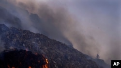 FILE - A person picks through trash for reusable items as a fire rages at the Bhalswa landfill in New Delhi, Apr. 27, 2022.