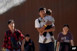 A group of people, including many from China, walk along the wall after crossing the border with Mexico to seek asylum, near Jacumba, California, Oct. 24, 2023.