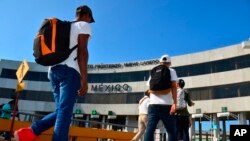FILE - US asylum-seekers being returned by U.S. authorities under the so-called Remain in Mexico program are escorted by a Mexican migration agent as they walk back into Mexico across the international bridge from Laredo, Texas, July 10, 2019.
