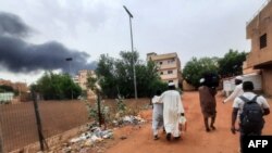 Smoke rises above buildings as people flee with some belongings, in Khartoum, Sudan, June 10, 2023. 