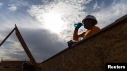 FILE - A construction worker drinks a cold beverage during a heat wave where temperatures rose to over 110 degrees Fahrenheit in Scottsdale, Ariz., July 28, 2023. A new study says climate change will cut incomes and also impact worker productivity.