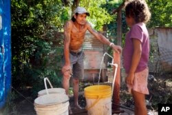 Carmelo Del Valle na binti yake waliolazimika kuhama makazi yao kutokana na mafuriko ya Mto Paraguay, wakiteka maji huko Asuncion, Paraguay, March 18, 2023.
