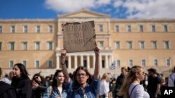 Seorang demonstran mengangkat plakat bertuliskan "Yunani memakan anak-anak mereka" saat protes untuk korban bencana kereta di depan Parlemen, Athena, 8 Maret 2023. (Foto: AP)