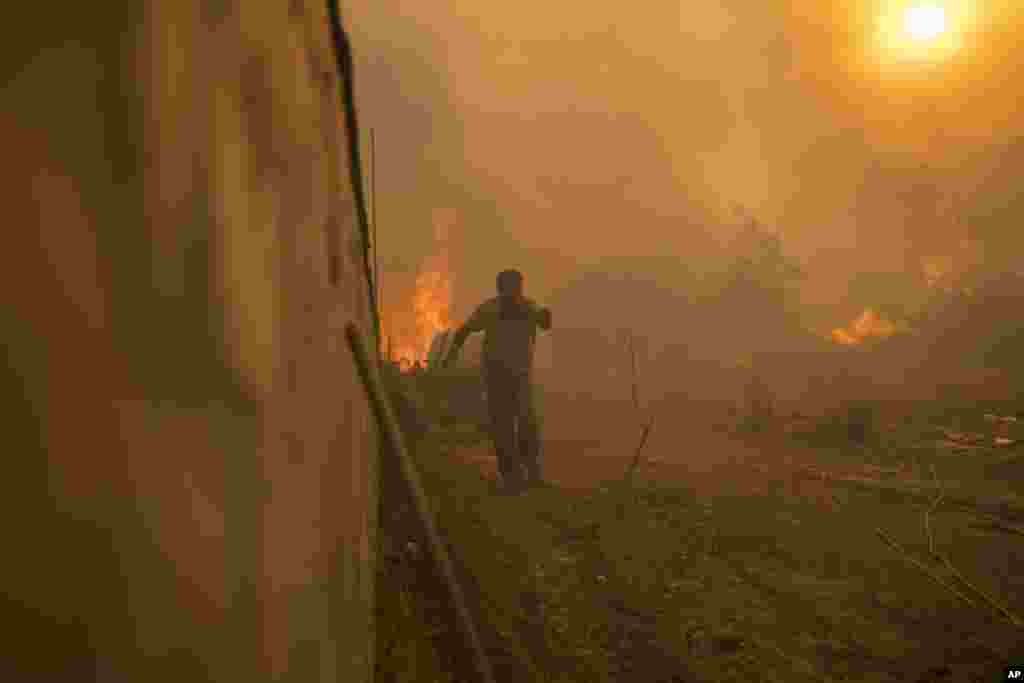 A local runs to avoid the flames of a wildfire in Gennadi village, on the Aegean Sea island of Rhodes, southeastern Greece, July 25, 2023.&nbsp;A firefighting plane has crashed in southern Greece, killing both crew members, as authorities are battling fires across the country amid a return of heat wave temperatures.