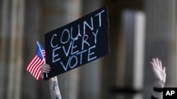 Seorang perempuan menunjukkan poster saat menghadiri rapat umum organisasi Demokrat di luar negeri setelah pemilihan umum di Amerika Serikat, di Berlin, Jerman, Rabu, 4 November 2020. (Markus Schreiber/AP)