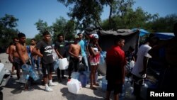 FILE - Asylum-seekers line up to refill their canisters with drinking water while they wait to attempt to cross into the U.S., at a makeshift camp in Matamoros, Mexico, June 19, 2023.