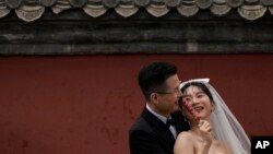 FILE - A bride and groom share a light moment with a sugar-coated Chinese haw as they pose during a pre-wedding photo shoot outside the Drum Tower in Beijing, April 23, 2023.