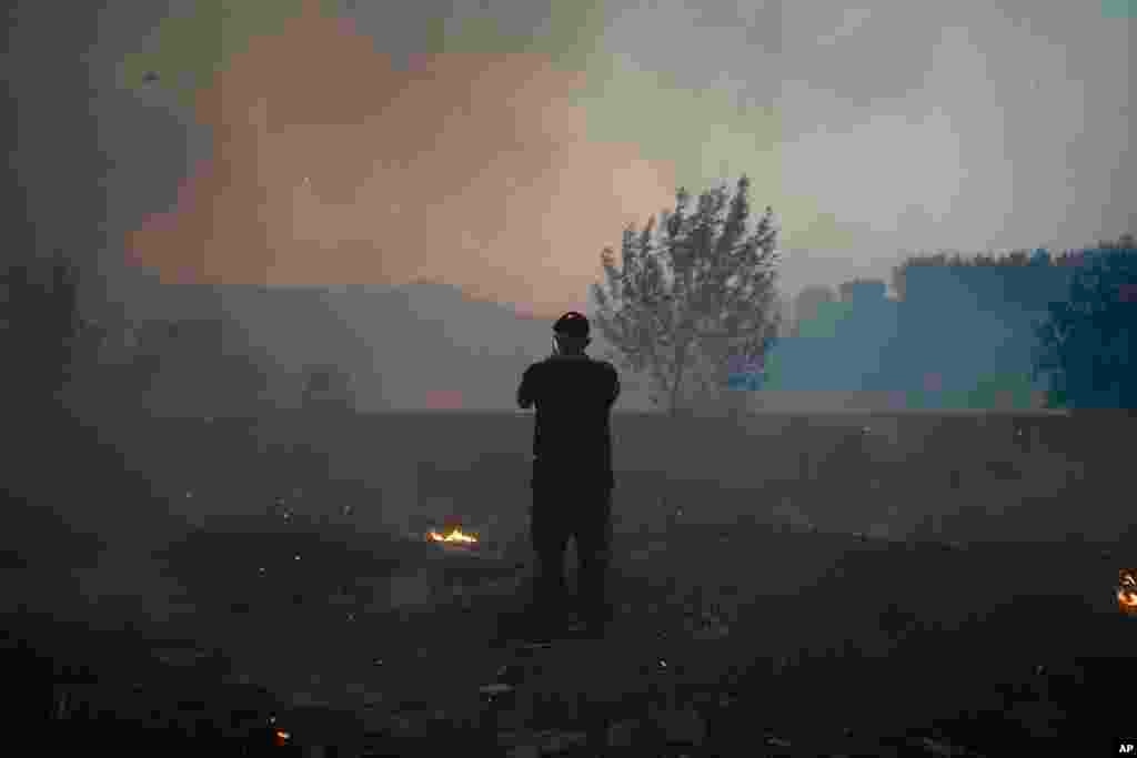 A man takes pictures of a wildfire as embers fly about him in Alcabideche, outside Lisbon, Portugal, July 25, 2023. 