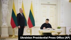 Lithuania's President Gitanas Nauseda, left, watches Ukrainian President Volodymyr Zelenskyy sign the guest book during their meeting in Vilnius, Lithuania, Jan. 10, 2024. (Ukrainian Presidential Press Office via AP)