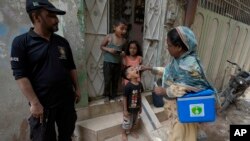 FILE - A police officer stands guard as a health worker administers a polio vaccine to a child at a neighborhood of Karachi, Pakistan, Monday, June 19, 2023.