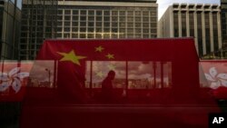 A pedestrian walking through a footbridge is silhouetted as Chinese and Hong Kong flags are strung to mark the 26th anniversary of the city's handover from Britain to China in Hong Kong, on June 27, 2023. 