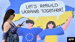 Žena prolazi pored plakata sa natpisom "Obnovimo Ukrajinu zajedno!" u centru ukrajinske prijestonice Kijeva, 24. maja 2023.