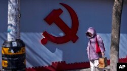 一名女子走过北京一处住宅小区围墙上的中共标识。（2024年3月1日）