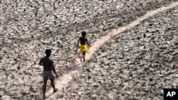 Seorang pria dan anak laki-laki berjalan di atas area sungai Yamuna yang mengering di New Delhi, India, pada 2 Mei 2022. (Foto: AP/Manish Swarup)