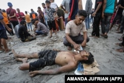Seorang pria memberikan air kepada pengungsi Rohingya yang baru tiba setelah dia berenang ke pantai sementara yang lain terdampar di perahu di Pineung, Aceh, 16 Oktober 2023. (Foto: AMANDA JUFRIAN/AFP)