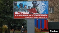 FILE - A local resident walks past a billboard encouraging men to join a Russian battalion amid Moscow's war on Ukraine, in Melitopol, Russian-occupied Ukraine, Nov. 27, 2022. Three Russian officers were reportedly killed in an attack Saturday on a local military headquarters.