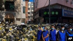 จนท.รักษาความปลอดภัยสวมเสื้อกั๊กสีน้ำเงินยืนดูแลความเรียบร้อยที่หน้ากองดอกไม้ที่ประชาชนนำมาวางไว้หน้า อาคารที่พักในวัยเยาว์ของอดีตนายกรัฐมนตรีหลี่ เค่อเฉียง ในเมืองเหอเฟย์ มณฑลอานฮุย ในวันที่ 2 พ.ย. 2566