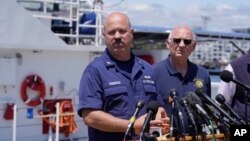 U.S. Coast Guard Capt. Jamie Frederick, left, faces reporters as Paul Hankins, U.S. Navy civilian contractor, supervisor of salvage, right, looks on during a news conference, June 21, 2023, at Coast Guard Base Boston, in Boston.