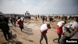 Sejumlah warga Palestina membawa kantung berisi terigu yang mereka ambil dari truk pembawa bantuan yang masuk ke Kota Gaza, pada 19 Februari 2024. (Foto: Reuters/Kosay Al Nemer)
