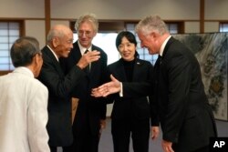 Toshihiro Mutsuda, second left, the elderly son of Japanese soldier Shigeyoshi Mutsuda, greets USS Lexington Museum executive director Steve Banta, right, before the handover ceremony of his father's flag, in Tokyo, Japan, on July 29, 2023. Mutsuda was only 5 years old when he last saw his father, who was drafted by Japan's Imperial Army in 1943 and killed in action.
