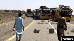 Orang-orang berjalan melewati truk pasokan yang diparkir di sepanjang jalan, setelah lalu lintas dihentikan menyusul serangan di jalan raya di provinsi Balochistan yang bergolak di Pakistan, 26 Agustus 2024. (Stringer/REUTERS)