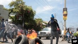 Seorang demonstran menyiramkan bensin ke arah ban yang terbakar dalam aksi protes menentang meningkatnya ketidakamanan di Haiti. Protes berlangsung di Port-au-Prince, Haiti, pada 17 September 2023. (Foto: AP/Odelyn Joseph)
