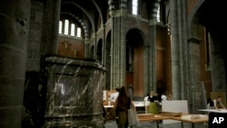 A woman walks by an art installation being set up at the Sacred Heart church in Mechelen, Beligum, June 19, 2023.