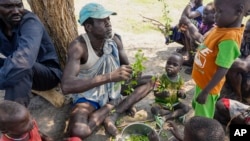 FILE - A displaced man and children rip leaves off branches, preparing to boil and eat them, in Kowach village in Canal Pigi county, Jonglei State, South Sudan, May 5, 2023. The country is due to hold presidential elections in 2024.