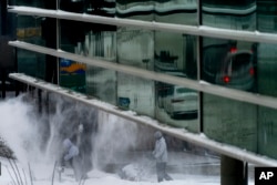 Men use snow blowers to clear a sidewalk in downtown Des Moines, Iowa, Jan. 13, 2024.