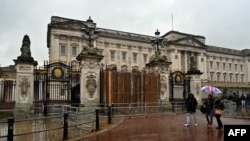 People walk past the a set of boarded up gates to Buckingham Palace in London, March 10, 2024, after a car crashed into them. 