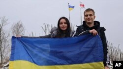 In this photo provided by the Ukrainian Presidential Press Office, Ukrainian teenager Bohdan Yermokhin, right, holds the Ukraine flag on the Ukraine-Belarus border, upon his return to Ukraine, Nov. 19, 2023. The young woman next to him was not identified.