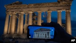 FILE - A woman holds up a mobile phone showing a digitally overlaid virtual reconstruction of the ancient Parthenon temple, at the Acropolis Hill in Athens, Greece on June 13, 2023.