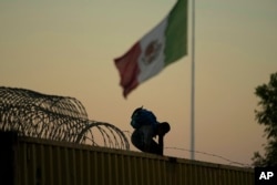 Seorang migran yang melintasi Rio Grande dari Meksiko ke AS harus bersusah payah melewati penghalang kawat berduri dan mobil boks di Eagle Pass, Texas, Jumat, 22 September 2023. (AP/Eric Gay)