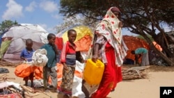 A woman walks with her children, who fled amid drought, to build a makeshift shelter at a camp for the displaced people on the outskirts of Mogadishu, Somalia, on Sept. 26, 2023. 