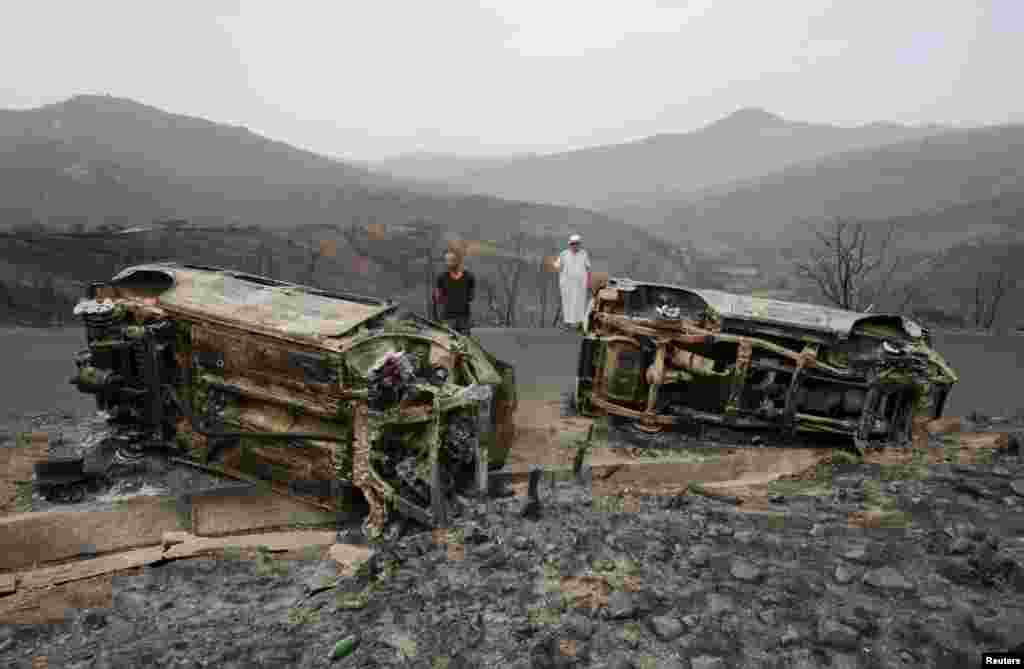 Men inspect burnt vehicles, in the aftermath of a wildfire in Bejaia, Algeria, July 25, 2023.