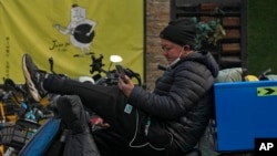 FILE - A man sits on his bike watching video from a social media app via his smartphone on a street in Beijing, Feb. 27, 2023. 
