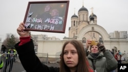 A woman holds a portrait of Alexey Navalny and his wife, Yulia, captioned "Eternal love has no death," outside the Church of the Icon of the Mother of God Soothe My Sorrows, where his funeral took place, in Moscow, Russia, March 1, 2024.