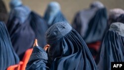 Afghan burqa-clad women sit as they wait to receive cash assistance being distributed by the World Food Program in Pul-i-Alam, the provincial capital of Logar Province, on Jan. 7, 2024. (Wakil KOHSAR / AFP)