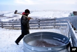 Tyson Ropp approaches a stock tank to break through the ice in a corral at the Double Cross Cattle Company ranch, Jan. 12, 2024, south of Roberts, Montana.