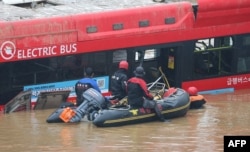 South Korean rescue workers search for missing persons near a bus along a deluged road leading to an underground tunnel where some 15 cars were trapped in flood waters after heavy rains in Cheongju, July 16, 2023. (Photo by YONHAP/AFP)