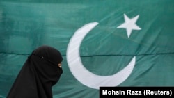 Seorang perempuan mengenakan burqa berjalan melewati bendera nasional Pakistan di Lahore 13 Agustus 2011. Pakistan mengatakan pada Rabu (17/1) bahwa Iran melakukan serangan udara di wilayahnya yang menewaskan dua anak. (Foto: REUTERS/Mohsin Raza)