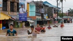 Warga mengarungi banjir yang dibawa hujan monsoon dan diperburuk oleh badai tropis Trami, di Cavite, bagian selatan Manila (19/8). (Reuters/Romeo Ranoco)