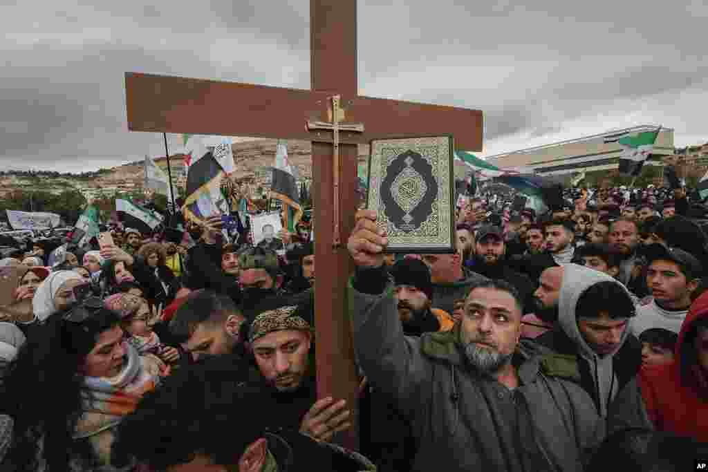 Syrians hold a copy of the Quran next to a Christian cross during a demonstration in support of unity among minorities and the ousting of the Bashar al-Assad government in Umayyad Square in Damascus, Syria.